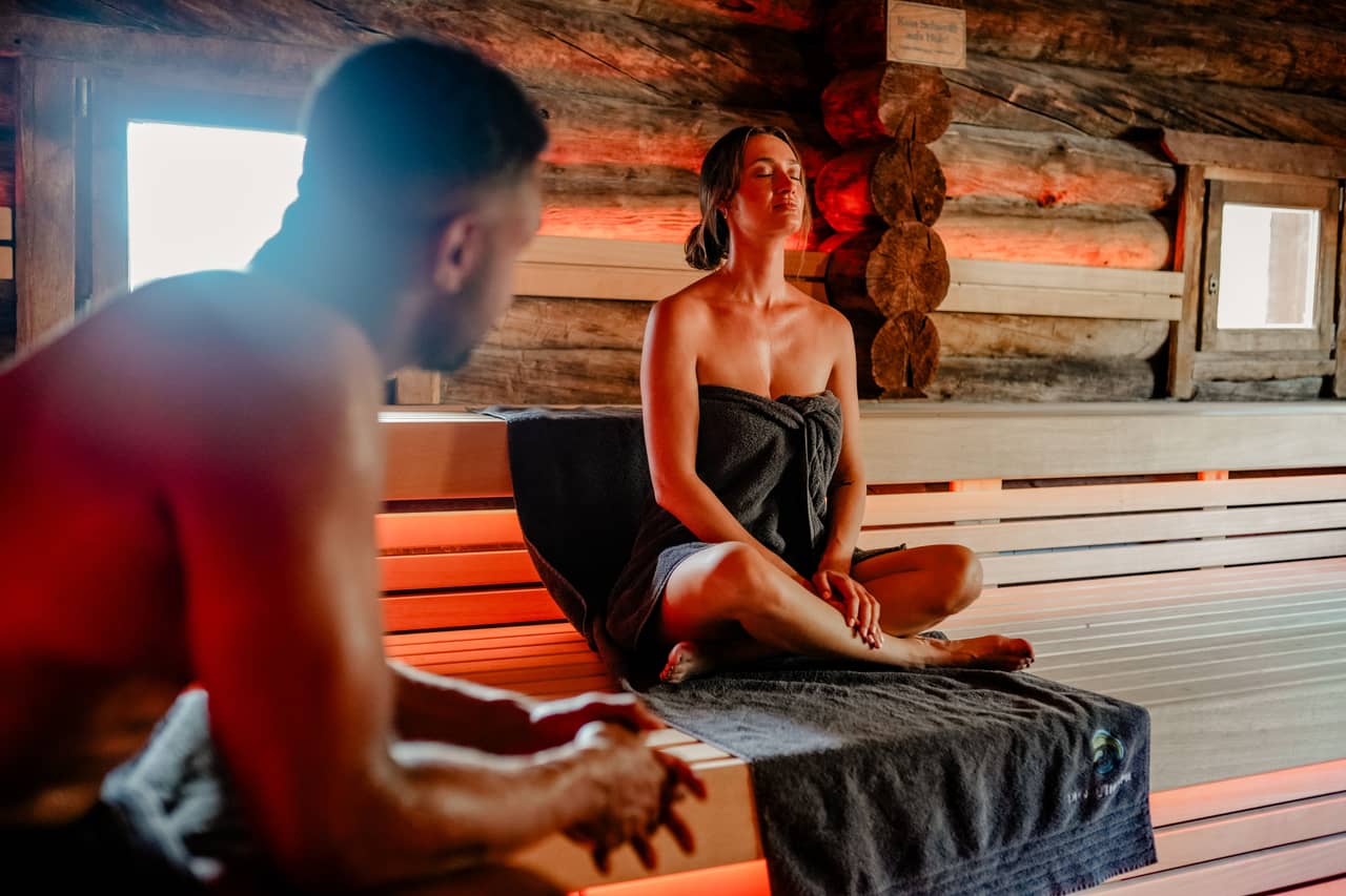 Frau und Mann sitzen in einer Sauna mit Handtuch.
